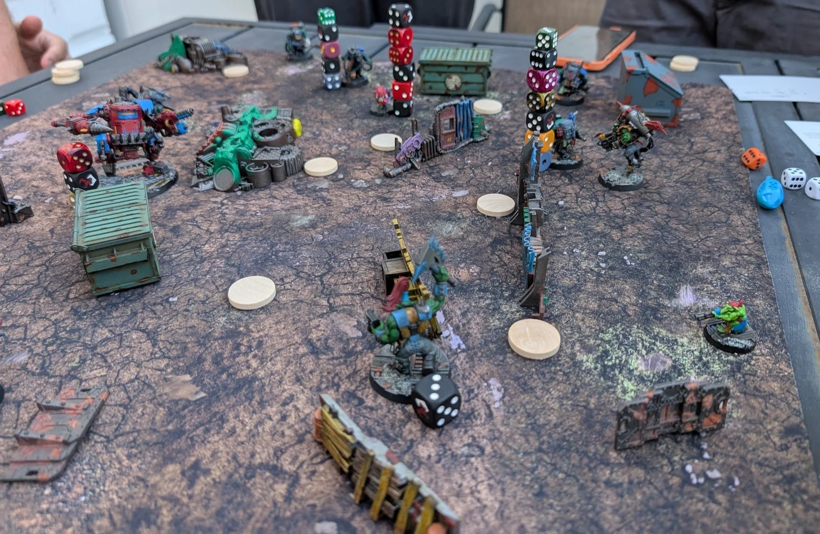 Three warbands of orks spread across a cracked-earth mat, several with dice towers stacked on their bases and wooden activation tokens scattered between them.