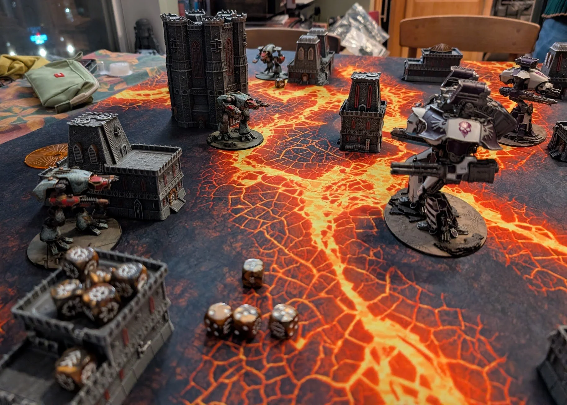 Adeptus Titanicus battlefield on a glowing lava mat: white and purple titans facing weathered green titans among gothic towers.