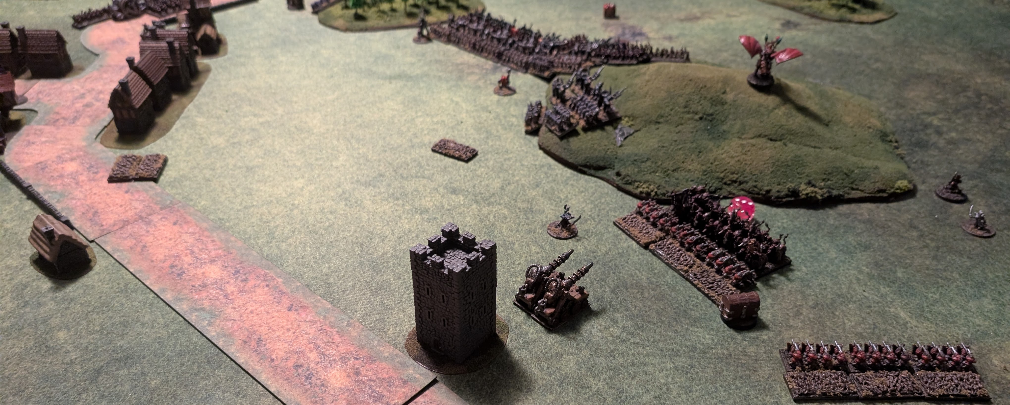 Warmaster battlefield in 10mm: massed Skaven blocks on a hill facing dark-armoured Chaos Dwarf regiments, with a stone tower and a village along the road.