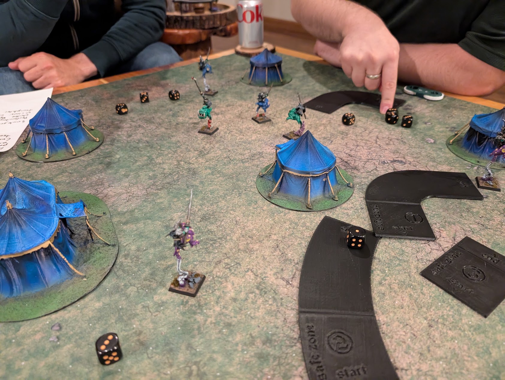Goblin jousting miniatures scatter among blue tents, with curved movement templates and dice on the table.